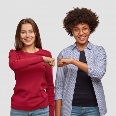 Multiethnic young women give fist bump to each other, show they are friendly team, have positive exp